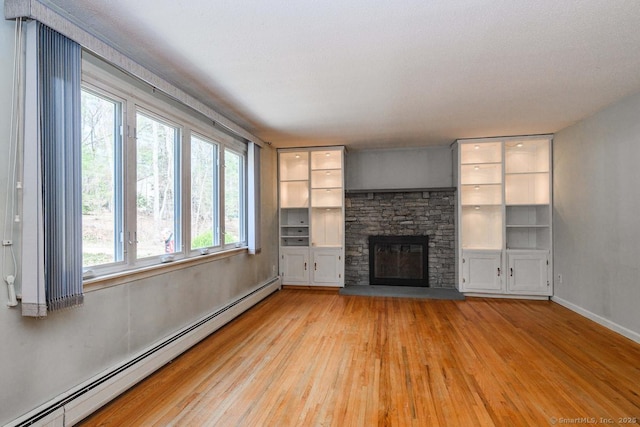 unfurnished living room with baseboards, built in shelves, a stone fireplace, light wood finished floors, and a baseboard heating unit