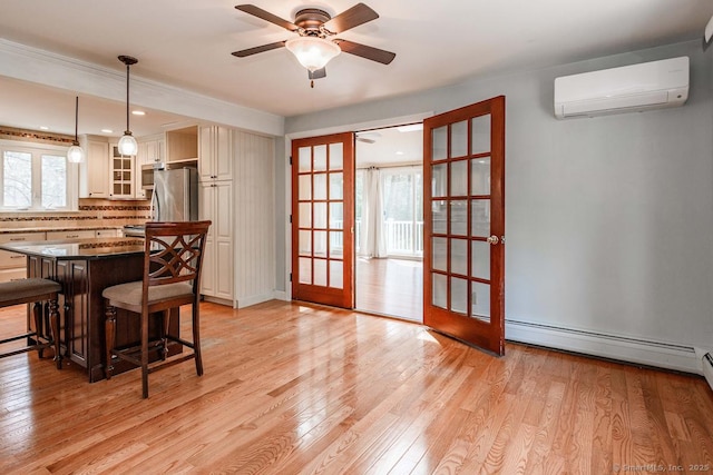 dining space featuring a wall mounted air conditioner, ceiling fan, light wood-type flooring, baseboard heating, and french doors