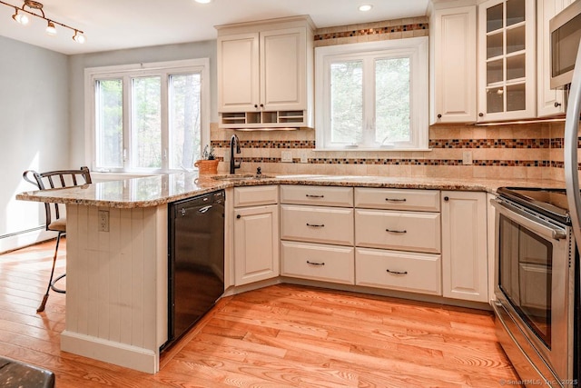 kitchen featuring stainless steel appliances, a peninsula, light wood-type flooring, and a sink