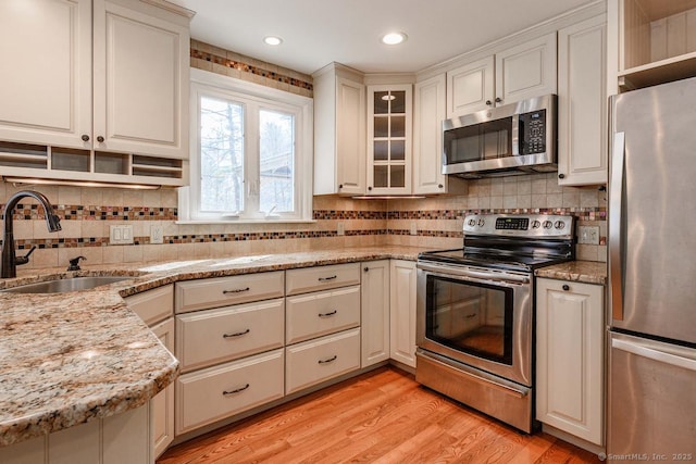 kitchen with appliances with stainless steel finishes, light wood-style flooring, open shelves, decorative backsplash, and a sink