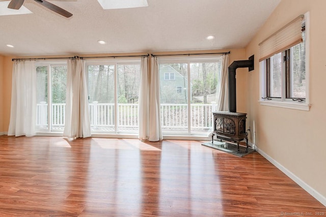 unfurnished living room with baseboards, a wood stove, ceiling fan, recessed lighting, and wood finished floors