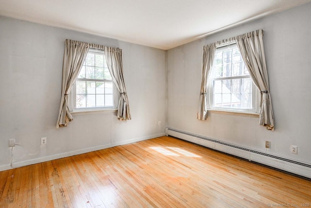empty room with a wealth of natural light, baseboards, a baseboard heating unit, and hardwood / wood-style floors