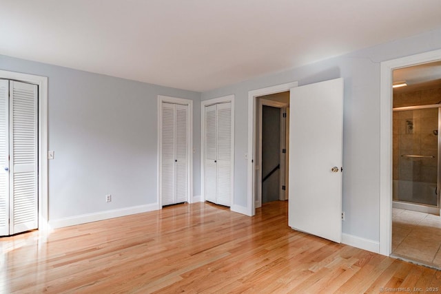 unfurnished bedroom with two closets, baseboards, and light wood-style floors