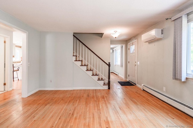 entrance foyer with stairs, a baseboard heating unit, wood finished floors, and a wall unit AC