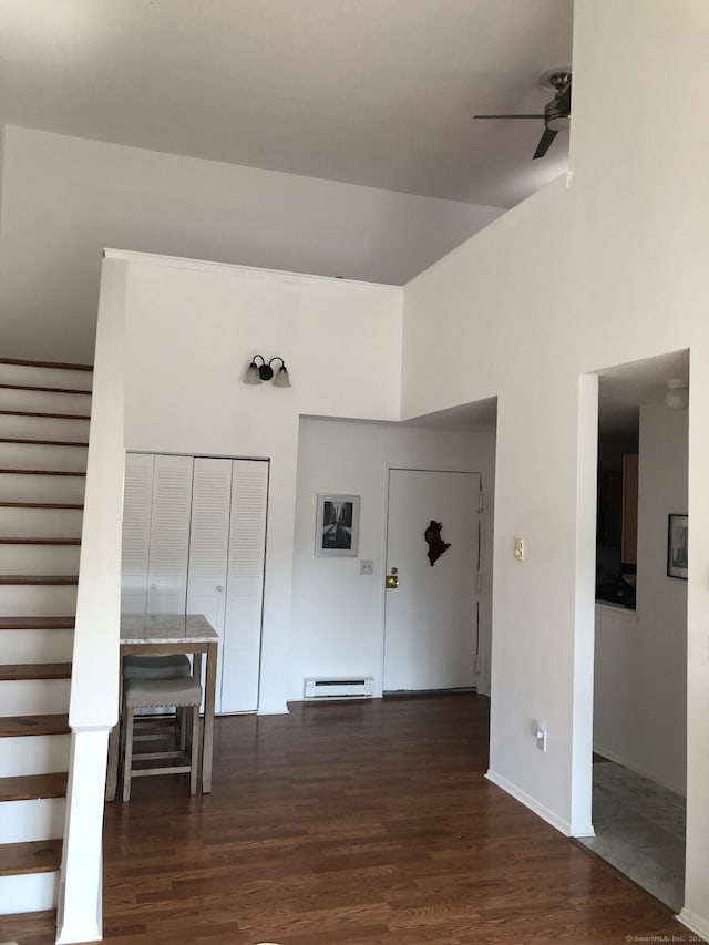 interior space with a baseboard heating unit, stairs, ceiling fan, and dark wood-style flooring