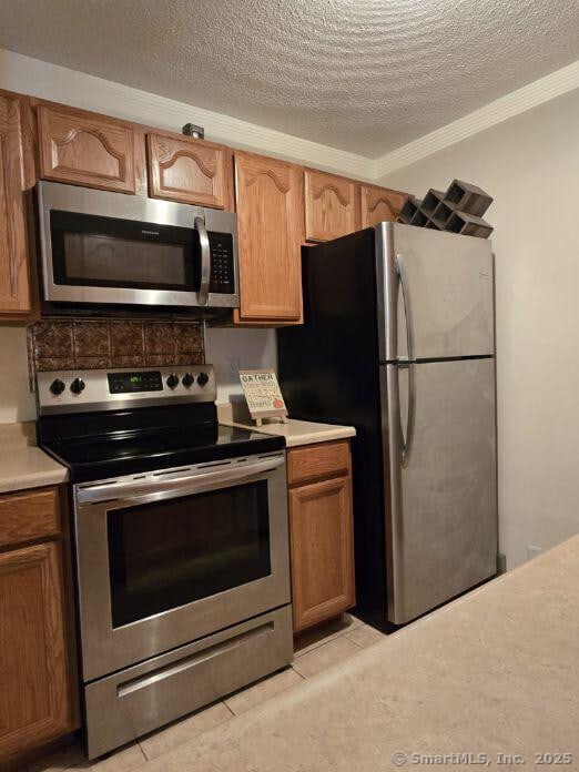 kitchen featuring ornamental molding, brown cabinetry, stainless steel appliances, and light countertops