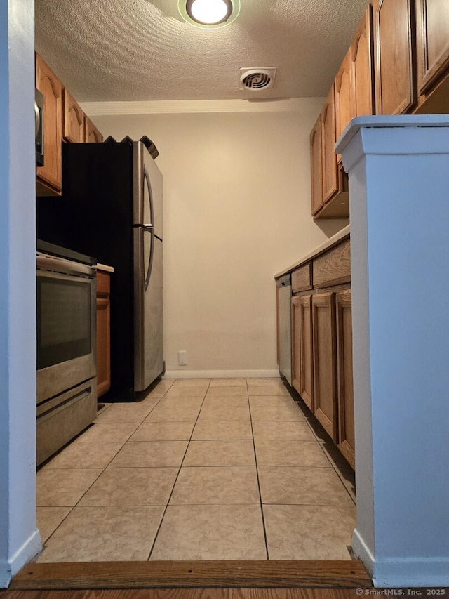 kitchen featuring light tile patterned floors, a textured ceiling, appliances with stainless steel finishes, and baseboards