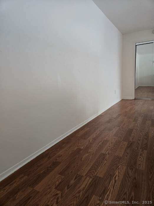 empty room with lofted ceiling, dark wood-type flooring, and baseboards