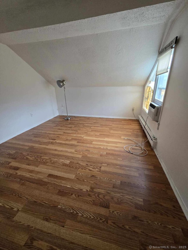 additional living space with a baseboard radiator, wood finished floors, and vaulted ceiling