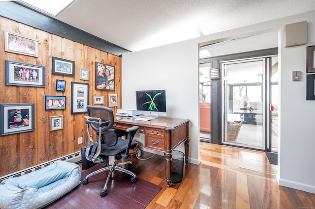 office space with baseboards, a textured ceiling, wood finished floors, and wood walls