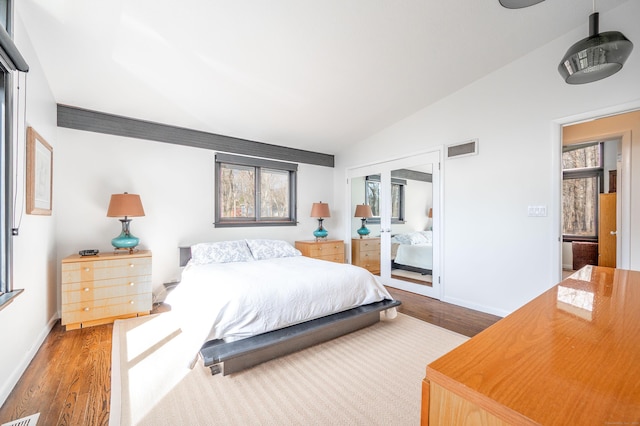 bedroom with wood finished floors, baseboards, lofted ceiling, and visible vents
