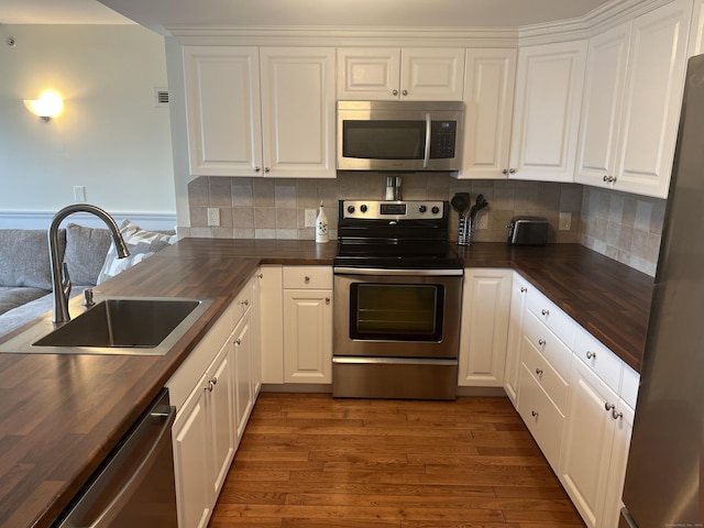 kitchen with a sink, butcher block counters, white cabinets, appliances with stainless steel finishes, and wood finished floors