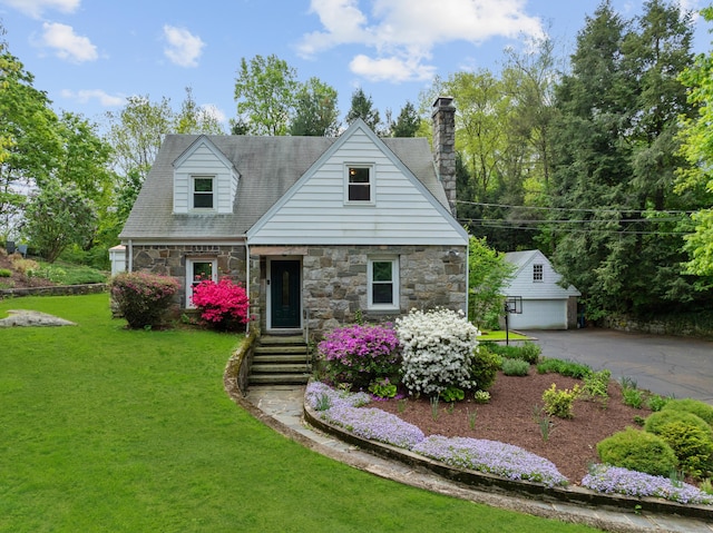 cape cod house with stone siding, an outbuilding, a front yard, a chimney, and a detached garage