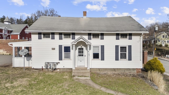 view of front of home featuring entry steps, a chimney, a front lawn, and roof with shingles