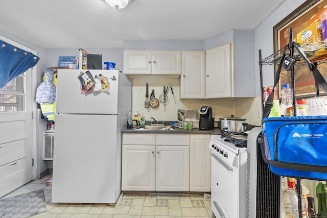 kitchen featuring white cabinetry, a sink, dark countertops, and white appliances