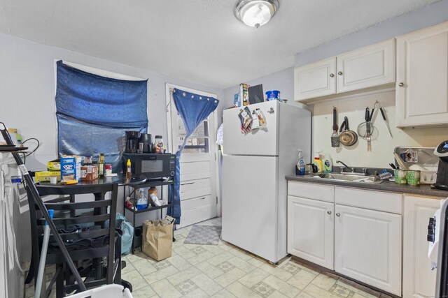 kitchen featuring a sink, freestanding refrigerator, black microwave, dark countertops, and white cabinets