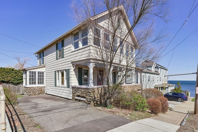 view of front facade featuring stone siding, driveway, and fence