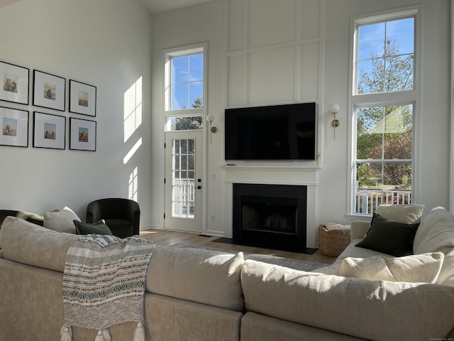 living area featuring wood finished floors, a fireplace with flush hearth, a high ceiling, and a wealth of natural light
