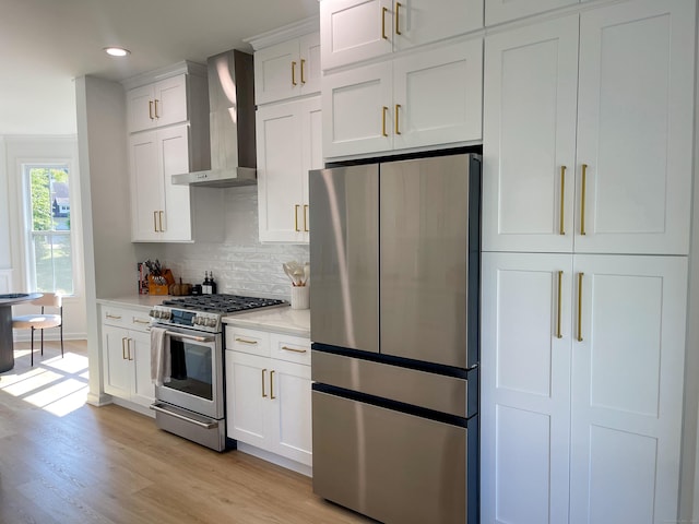 kitchen featuring light wood-style flooring, wall chimney exhaust hood, stainless steel appliances, white cabinetry, and decorative backsplash