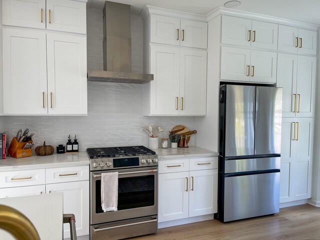 kitchen featuring wall chimney range hood, light wood-type flooring, white cabinetry, tasteful backsplash, and stainless steel appliances