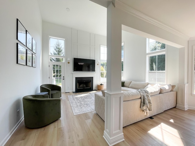 living room featuring a fireplace with flush hearth, baseboards, crown molding, and light wood-style flooring
