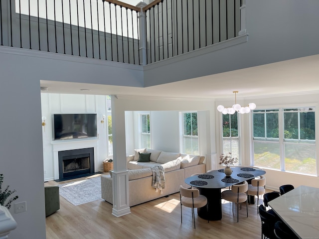 living area with a fireplace, an inviting chandelier, light wood finished floors, and a towering ceiling