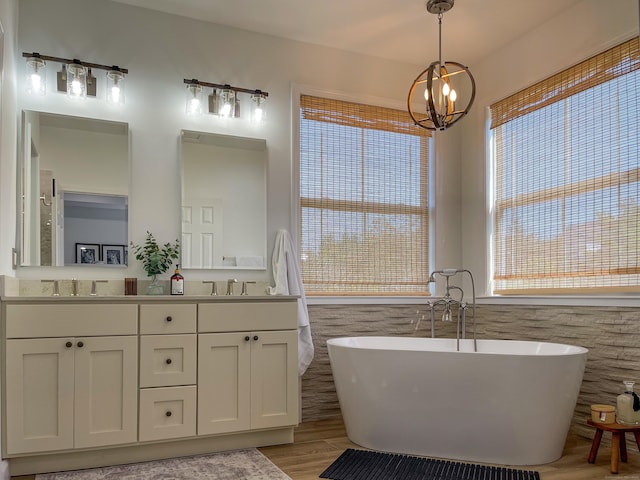 bathroom featuring double vanity, wood finished floors, a freestanding bath, a sink, and a notable chandelier