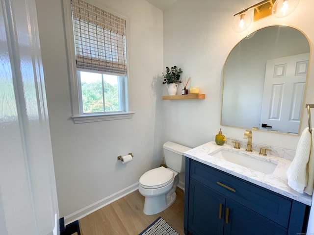 half bathroom featuring toilet, baseboards, wood finished floors, and vanity