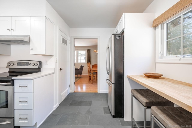 kitchen featuring stainless steel appliances, light countertops, white cabinets, under cabinet range hood, and dark tile patterned floors