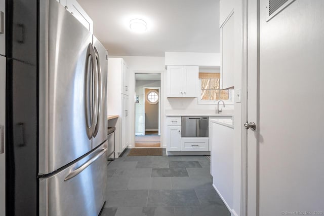 kitchen with white cabinets, light countertops, a sink, dark tile patterned floors, and appliances with stainless steel finishes
