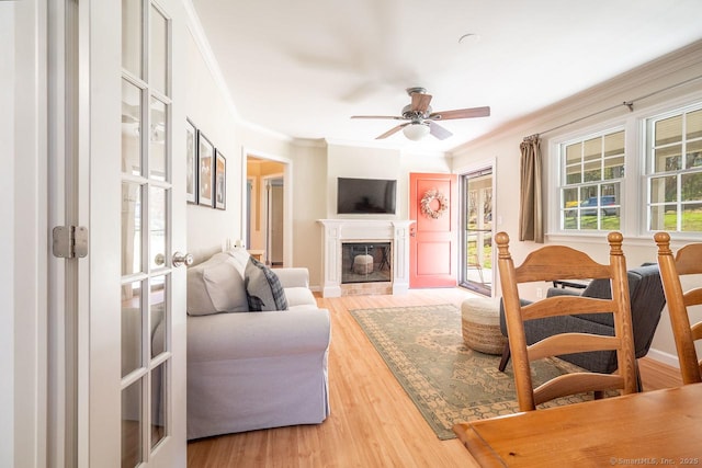 living area with a tile fireplace, a ceiling fan, ornamental molding, and light wood-style floors