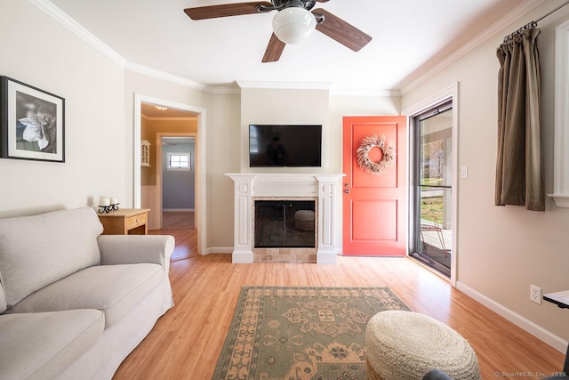 living area featuring light wood finished floors, baseboards, a glass covered fireplace, ceiling fan, and crown molding