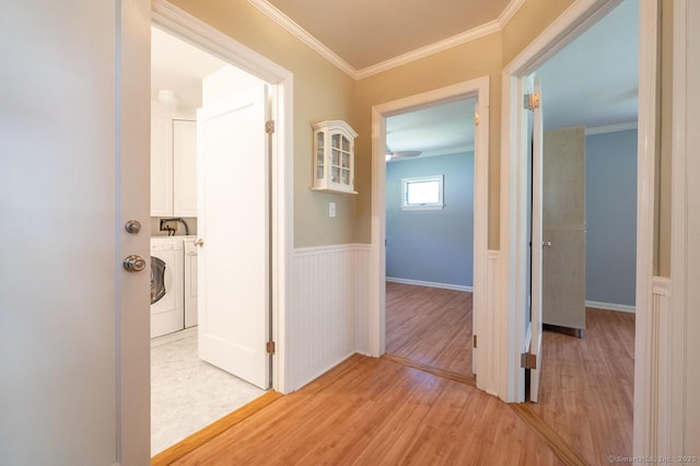 hallway with washing machine and clothes dryer, crown molding, a wainscoted wall, and light wood-style flooring