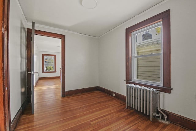 spare room featuring radiator heating unit, baseboards, ornamental molding, and wood finished floors