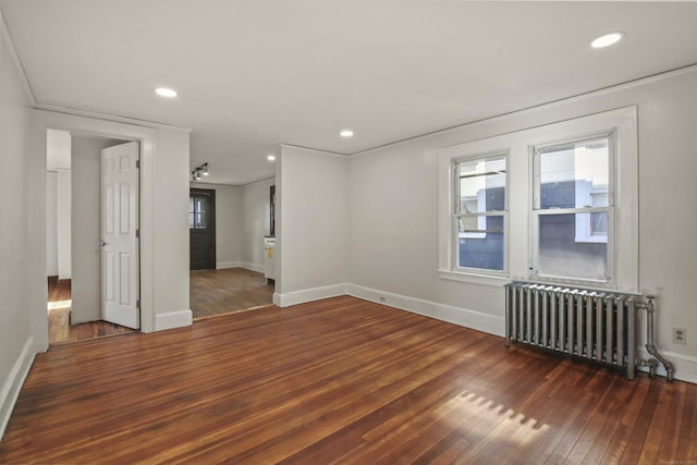 spare room featuring radiator, wood-type flooring, baseboards, and plenty of natural light
