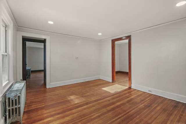 empty room with baseboards, recessed lighting, radiator, and wood finished floors