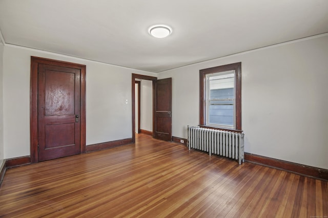 unfurnished room with radiator heating unit, wood-type flooring, baseboards, and crown molding