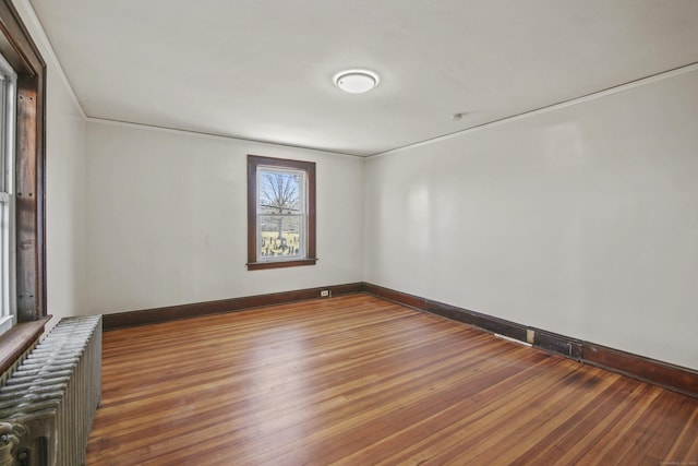 spare room featuring baseboards, crown molding, radiator, and wood finished floors