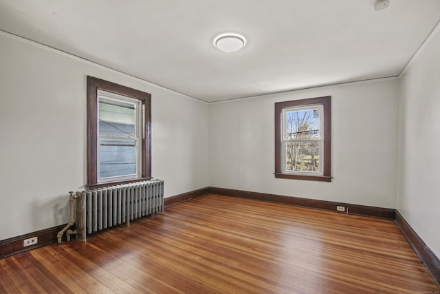 empty room featuring baseboards, hardwood / wood-style floors, radiator, and crown molding