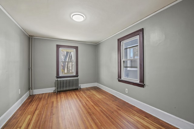 spare room with radiator heating unit, baseboards, hardwood / wood-style floors, and crown molding