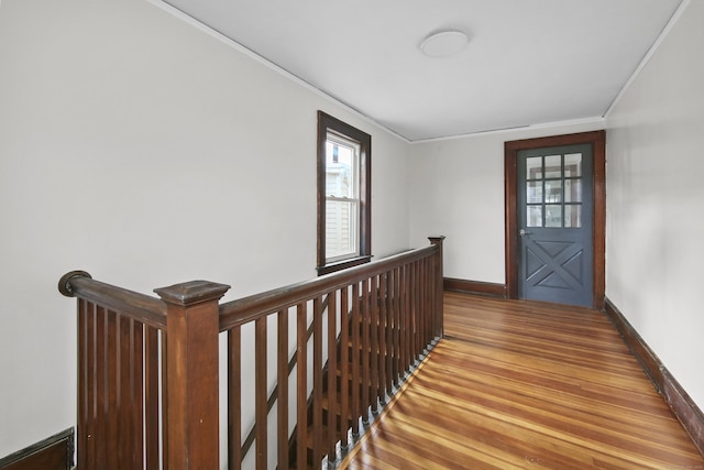 hallway featuring wood finished floors, baseboards, ornamental molding, and an upstairs landing