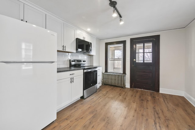 kitchen with radiator heating unit, white cabinets, appliances with stainless steel finishes, baseboards, and backsplash