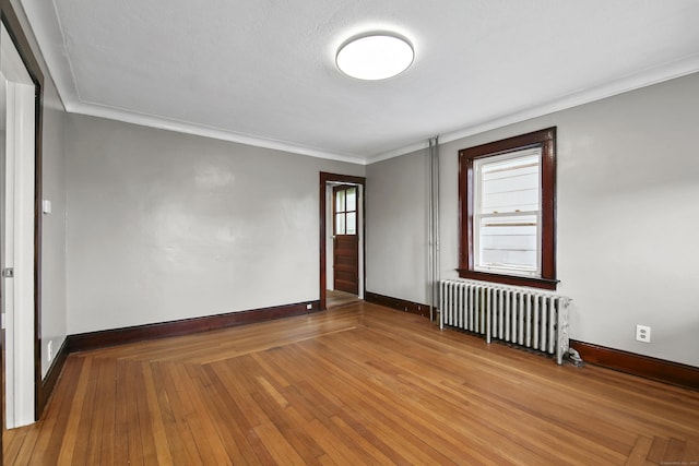 unfurnished room with baseboards, ornamental molding, radiator, and wood finished floors