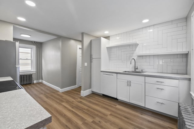 kitchen with baseboards, freestanding refrigerator, radiator, white dishwasher, and a sink
