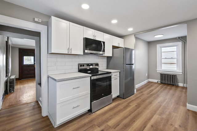 kitchen featuring baseboards, light countertops, radiator, wood finished floors, and stainless steel appliances