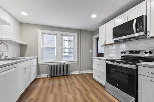 kitchen featuring baseboards, a sink, light wood-type flooring, appliances with stainless steel finishes, and radiator heating unit