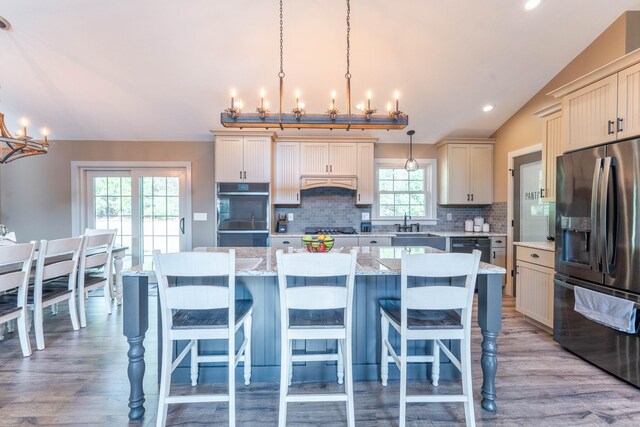kitchen with an inviting chandelier, appliances with stainless steel finishes, premium range hood, vaulted ceiling, and a kitchen island