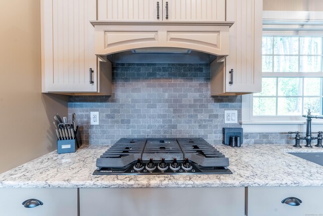kitchen with custom range hood, light stone countertops, stainless steel gas cooktop, decorative backsplash, and a sink