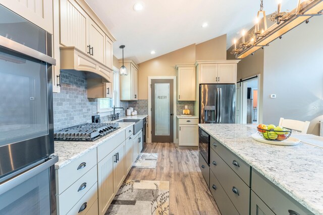 kitchen with a sink, appliances with stainless steel finishes, light wood-style floors, vaulted ceiling, and pendant lighting