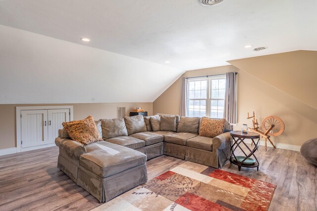 living area with visible vents, baseboards, vaulted ceiling, and wood finished floors